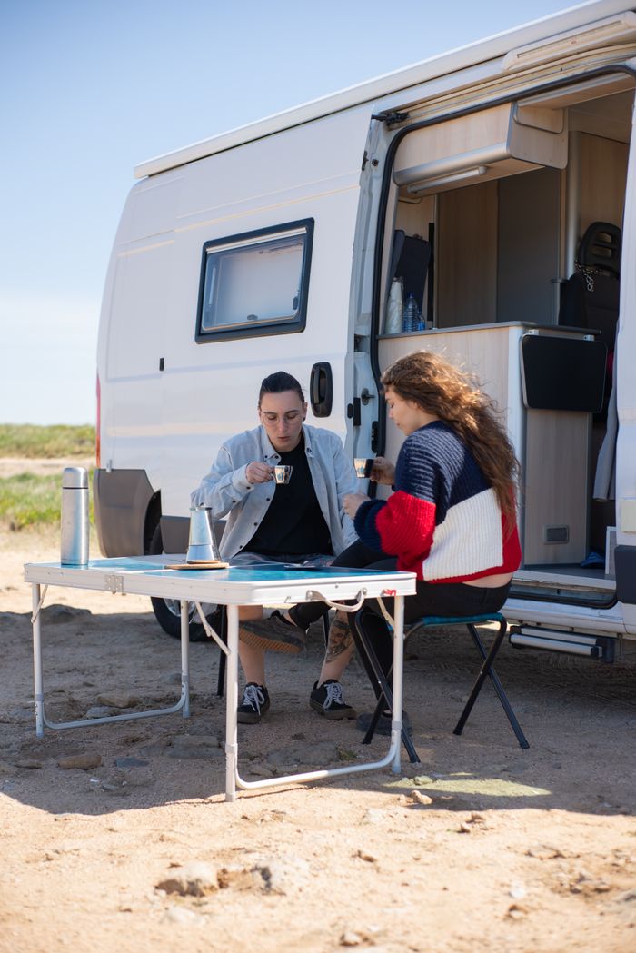 about-03 Two adults enjoying coffee by a campervan on a sunny beach in Portugal.